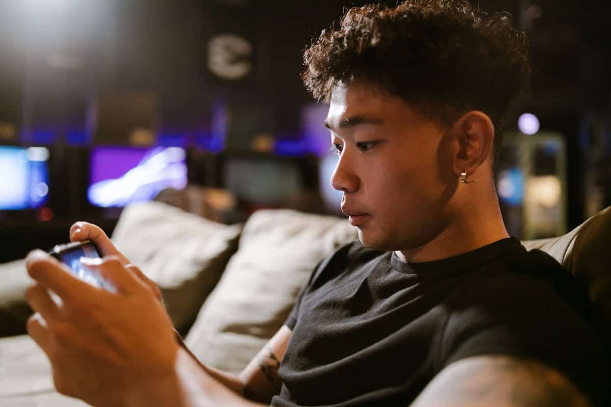 Close-up of a young Asian man immersed in mobile gaming indoors, highlighting modern technology and recreation.